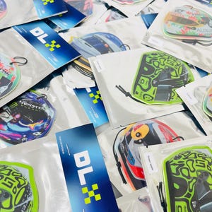 Puede incluir: Una variedad de ambientadores para coche con diferentes dise&ntilde;os, incluyendo un casco verde y negro, un casco rojo y blanco y un casco azul y blanco. Los ambientadores est&aacute;n empaquetados en bolsas de pl&aacute;stico transparentes con una etiqueta azul y blanca que dice "DLX".