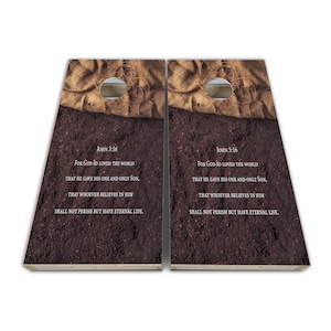 May include: Two wooden cornhole boards with a burlap and dirt background. The boards have a hole in the center and the text "John 3:16" and a bible verse printed on them.