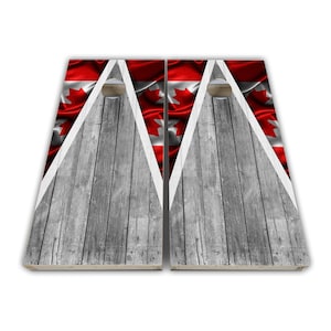 Könnte beinhalten: Zwei hölzerne Cornhole-Bretter mit einem kanadischen Flaggen-Design. Die Bretter sind mit einem verwitterten Holzeffekt bemalt und haben auf jeder Seite ein weißes Dreieck mit einem roten Ahornblatt.