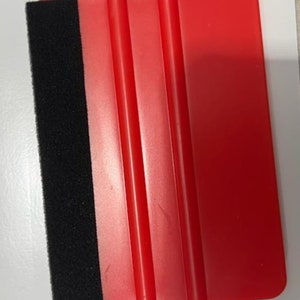May include: A red plastic squeegee with a black felt edge. The squeegee has three raised ridges on the red surface.
