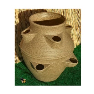 May include: A brown ceramic planter with multiple openings for planting herbs or small plants. The planter has a rounded shape and a textured surface.