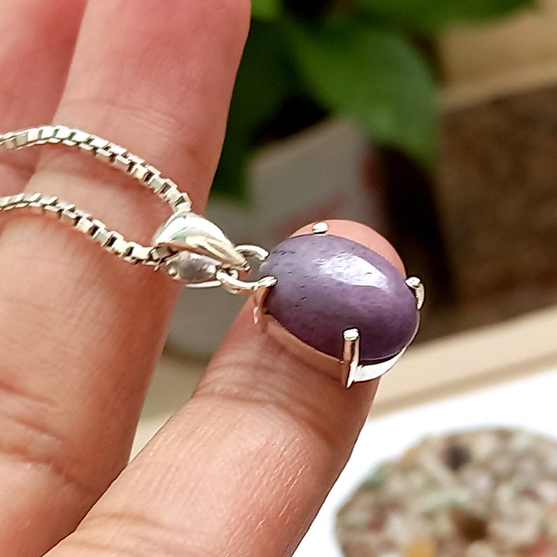 May include: A silver pendant with a purple oval gemstone set in a silver bezel. The pendant is on a silver chain.