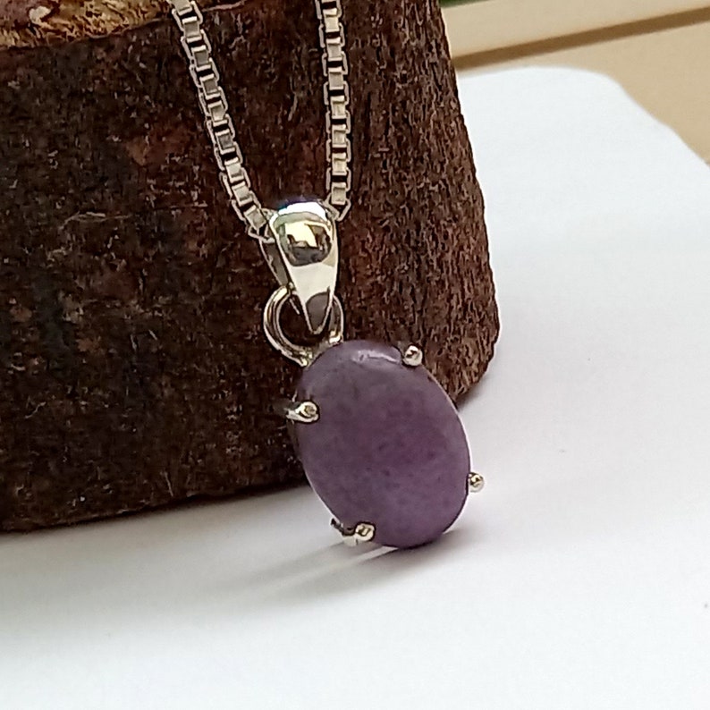 May include: A silver chain necklace with a pendant featuring a purple oval gemstone set in a silver bezel.
