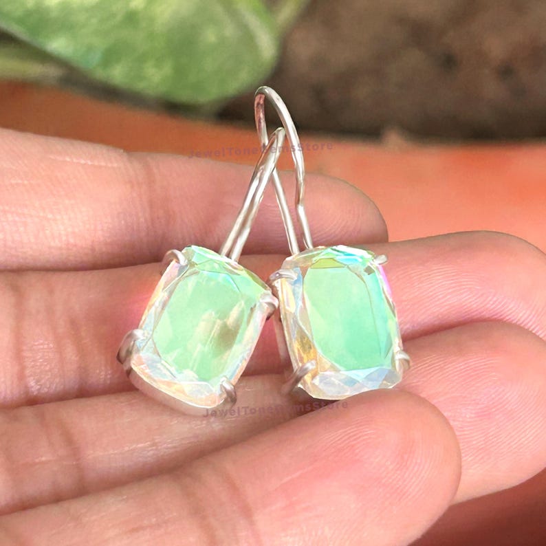 May include: A pair of drop earrings featuring rectangular, faceted, iridescent light green stones set in silver-toned metal prongs. Each earring hangs from a simple curved silver-toned wire hook, showcasing a reflective, shimmering surface.