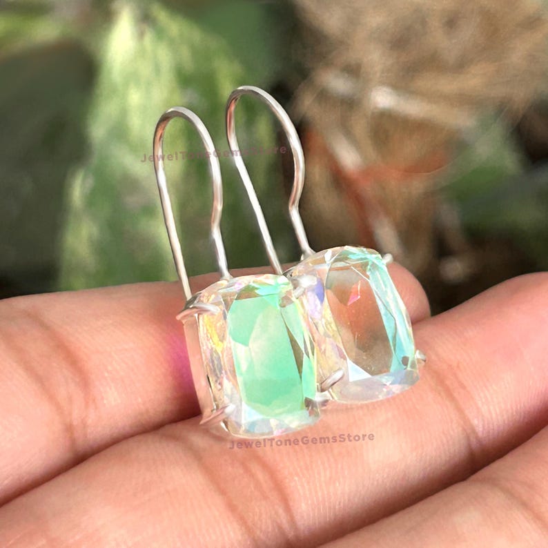 May include: A pair of silver-toned hook earrings featuring rectangular, faceted iridescent stones that display shifting hues of green, blue, and pink. The stones are held in a simple metal setting with a clear, reflective, and prismatic surface finish.