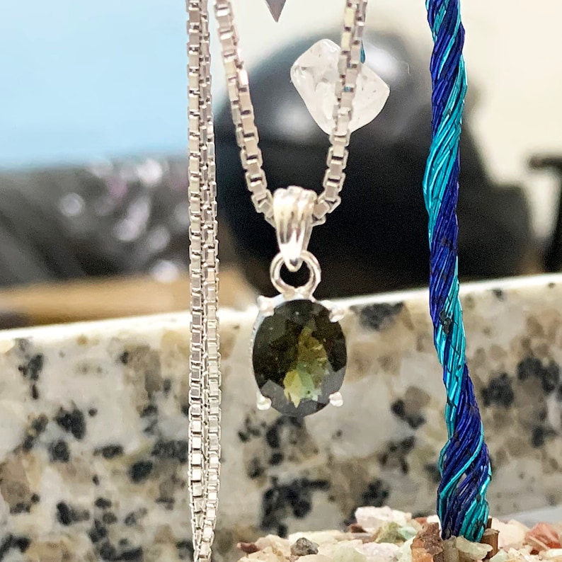 Op de afbeelding: Een zilveren ketting met een hanger met een donkergroene ovale edelsteen. De hanger zit aan een zilveren ketting met een box chain-ontwerp.
