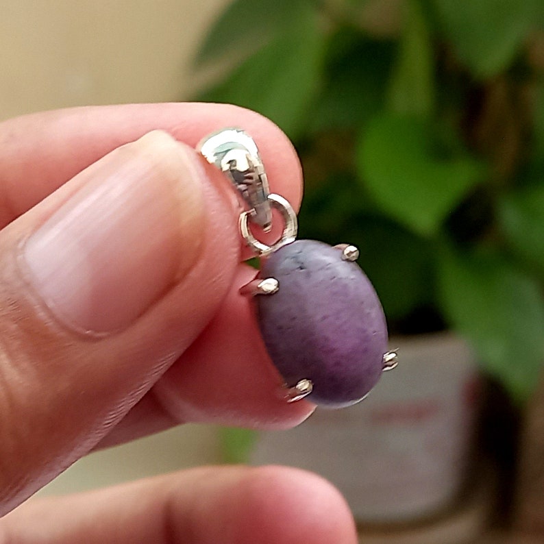 May include: A silver pendant with a purple gemstone. The gemstone is oval shaped and has a smooth, polished surface.
