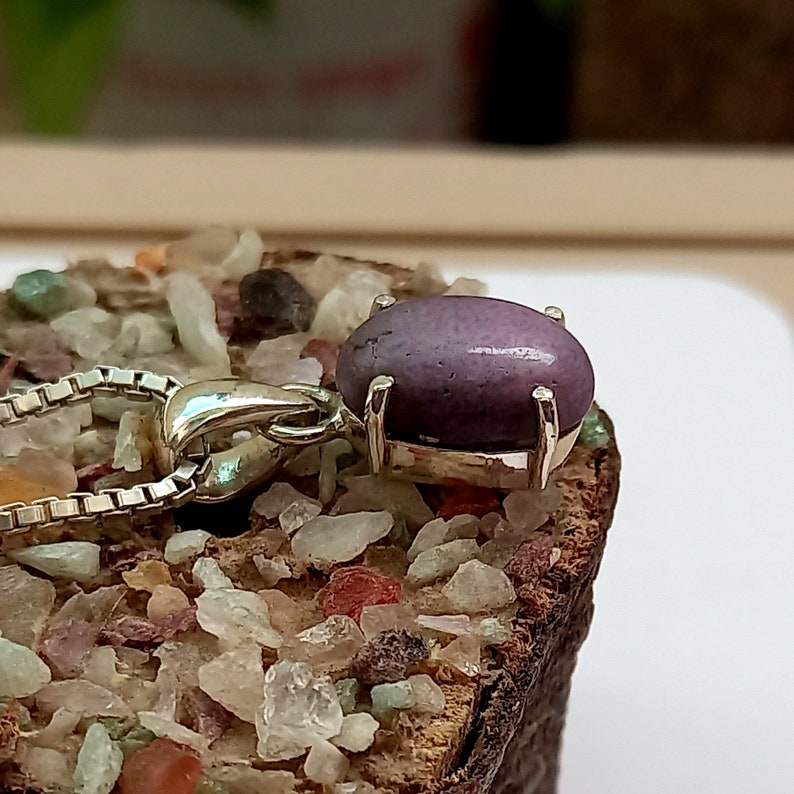 May include: A silver pendant with a purple gemstone set in a silver bezel. The pendant is attached to a silver chain.