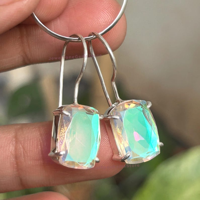 May include: A pair of silver-toned drop earrings featuring rectangular, faceted iridescent stones that display shifting green and pink hues. The stones are held in four-prong settings attached to curved silver-toned ear wires for a secure fit.