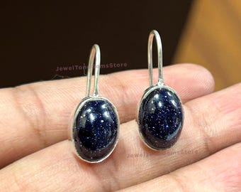 May include: A pair of silver dangle earrings with oval-shaped blue gemstone stones. The stones have a sparkly, speckled texture.