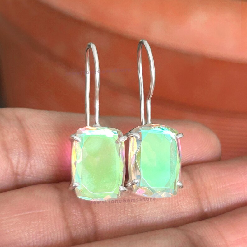 May include: A pair of drop earrings featuring rectangular, faceted, iridescent light green stones set in silver-toned metal prongs. The earrings have long, curved silver-toned ear wires that extend upward from the top of each stone setting.