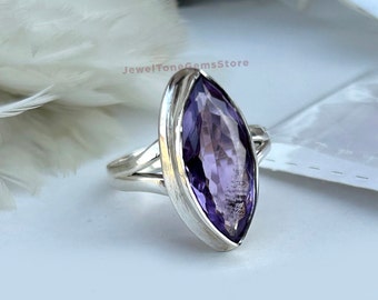 May include: A silver ring with a large, marquise-shaped amethyst gemstone. The ring has a delicate, twisted band.