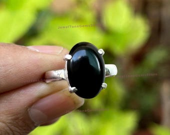 May include: A silver ring with a large, oval-shaped black gemstone. The ring is set with small silver accents around the gemstone.