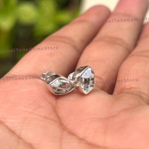 Peut inclure: Une paire de boucles d'oreilles en argent avec des pierres précieuses facettées transparentes. Les boucles d'oreilles sont serties dans un style simple et moderne.