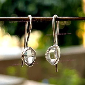 May include: A pair of silver earrings featuring clear, faceted, octagonal gemstones. The earrings have a simple, elegant design.