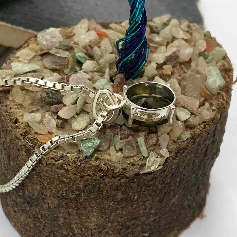 Op de afbeelding: Een zilveren ketting met een hanger met een ronde, donkergroene edelsteen in een zilveren zetting.