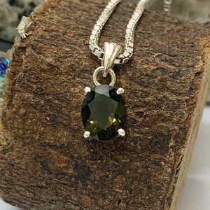 Op de afbeelding: Een zilveren ketting met een hanger met een donkergroene ovale edelsteen.