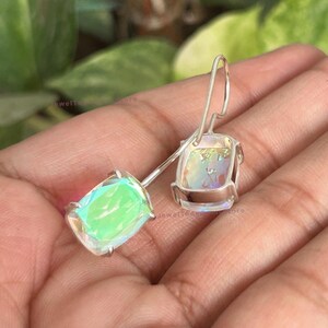 May include: A pair of silver drop earrings featuring rectangular, iridescent stones that display shifting green and pink hues. Each stone is held in a simple four-prong setting attached to a curved silver ear wire, creating a clean, reflective look.