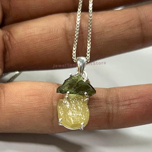 Puede incluir: Un collar de cadena de plata con un colgante con una piedra preciosa verde y amarilla. El colgante está engastado en plata y tiene una forma única e irregular.