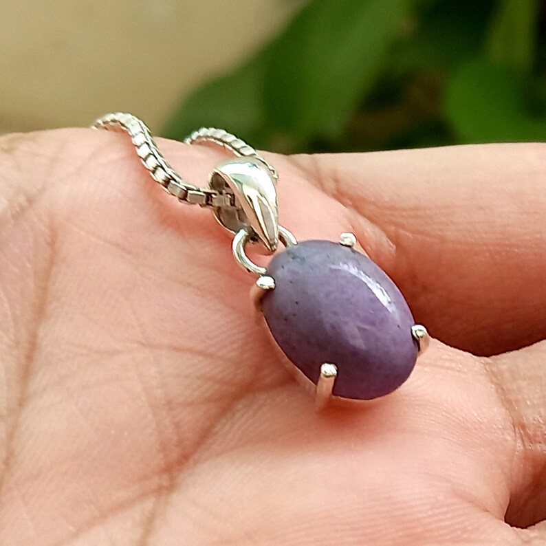 May include: A silver pendant with a purple oval gemstone. The pendant is on a silver chain.