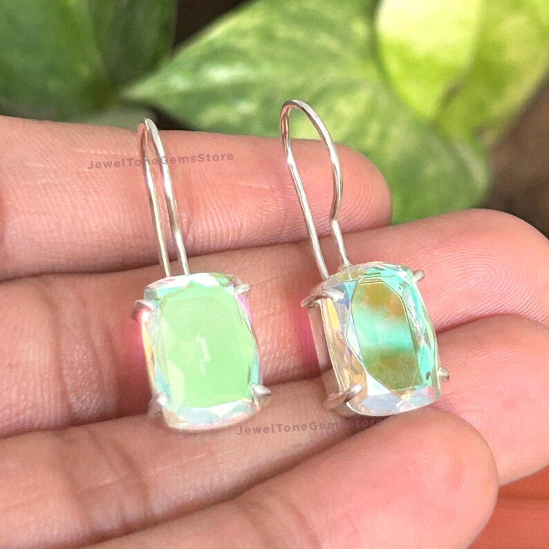 May include: A pair of drop earrings featuring rectangular, faceted, iridescent light green stones set in silver-toned metal prongs with curved ear wires. The stones display a shifting color effect with hints of yellow and blue light reflections.