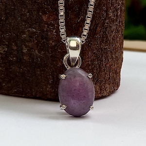 May include: A silver chain necklace with a purple gemstone pendant. The pendant is oval shaped and has a silver setting.