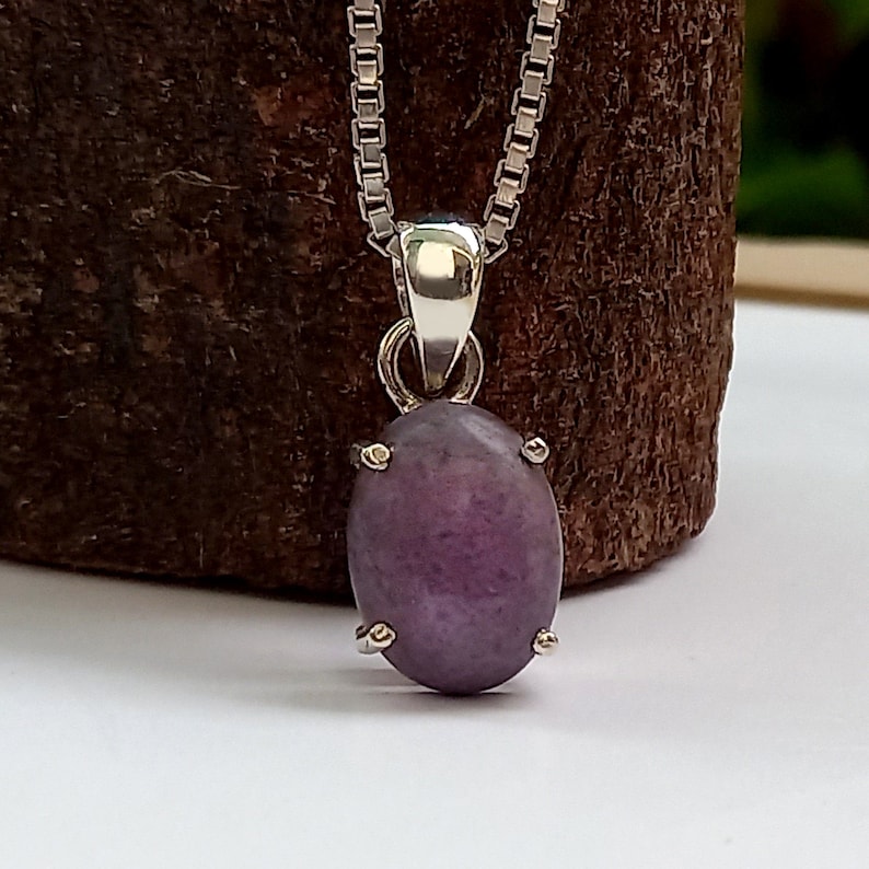 May include: A silver chain necklace with a purple gemstone pendant. The pendant is oval shaped and has a silver setting.