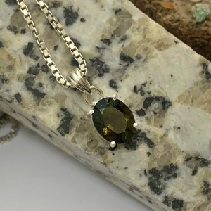 Op de afbeelding: Een zilveren ketting met een hanger met een donkergroene ovale edelsteen.
