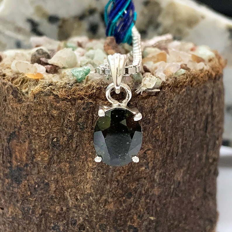 Op de afbeelding: Een zilveren hanger met een donkergroene ovale edelsteen. De hanger zit aan een zilveren ketting.