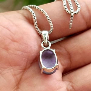 May include: A silver chain necklace with a pendant featuring a purple oval gemstone.