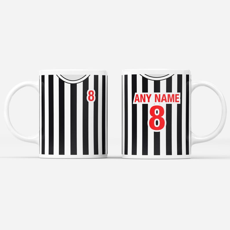 Puede incluir: Dos tazas de cer&aacute;mica blanca con un dise&ntilde;o a rayas blancas y negras, que se asemeja a una camiseta deportiva. Una taza presenta el n&uacute;mero 8 en rojo, mientras que la otra tiene "ANY NAME" encima del n&uacute;mero 8. Las tazas tienen un asa blanca.