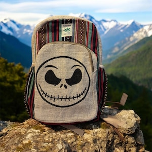 Puede incluir: Mochila de c&aacute;&ntilde;amo con la cara de Jack Skellington en el bolsillo delantero. La parte superior de la mochila tiene un dise&ntilde;o estampado con rayas rojas, verdes y marrones. Monta&ntilde;as en el fondo.