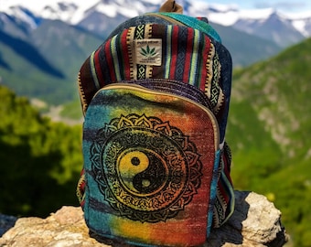 Könnte beinhalten: Ein farbenfroher Rucksack mit einem Yin-Yang-Symbol und einem Pure Hemp-Etikett. Der Rucksack hat ein Regenbogen-Tie-Dye-Design auf der Vorderseite und Streifenmuster an den Seiten. Im Hintergrund ist ein Gebirge zu sehen.