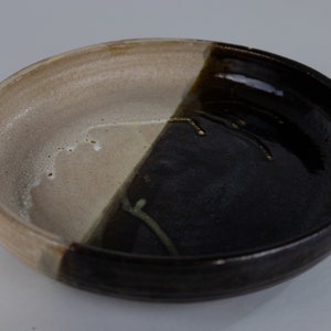 May include: A ceramic bowl with a white and black glaze. The bowl is divided in half, with one side being white and the other side being black. The black side has a glossy finish, while the white side has a matte finish.
