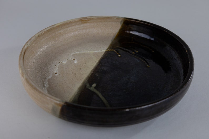 May include: A ceramic bowl with a white and black glaze. The bowl is divided in half, with one side being white and the other side being black. The black side has a glossy finish, while the white side has a matte finish.