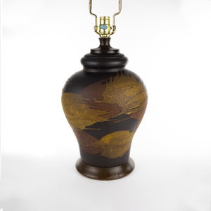 May include: A brown ceramic table lamp with a gold and brown abstract design. The lamp has a black base and a gold metal shade.