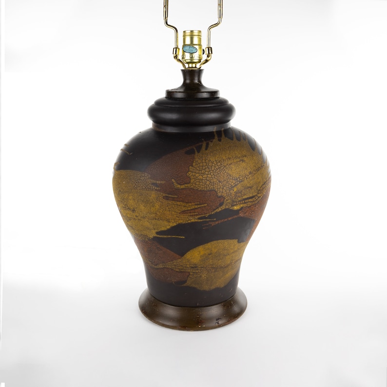 May include: A brown ceramic table lamp with a gold and brown abstract design. The lamp has a black base and a gold metal shade.
