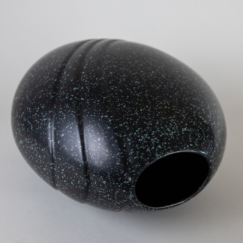 May include: A black and green speckled ceramic vase with a rounded, oval shape. The vase has a wide opening at the top.