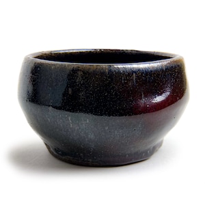 May include: A small, dark brown ceramic bowl with a glossy finish. The bowl has a slightly rounded shape and a wide rim.
