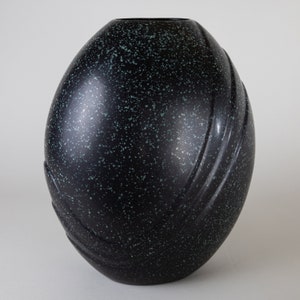 May include: A black and green speckled ceramic vase with a rounded, egg-shaped design and subtle grooves.
