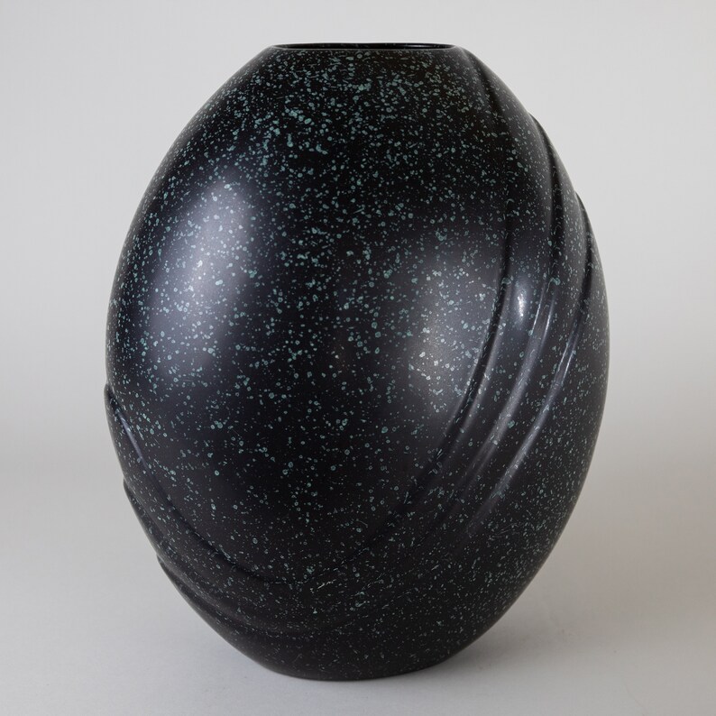 May include: A black and green speckled ceramic vase with a rounded, egg-shaped design and subtle grooves.