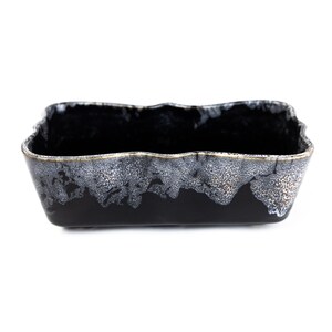 May include: A black ceramic planter with a wavy rim and a white and gold speckled glaze.
