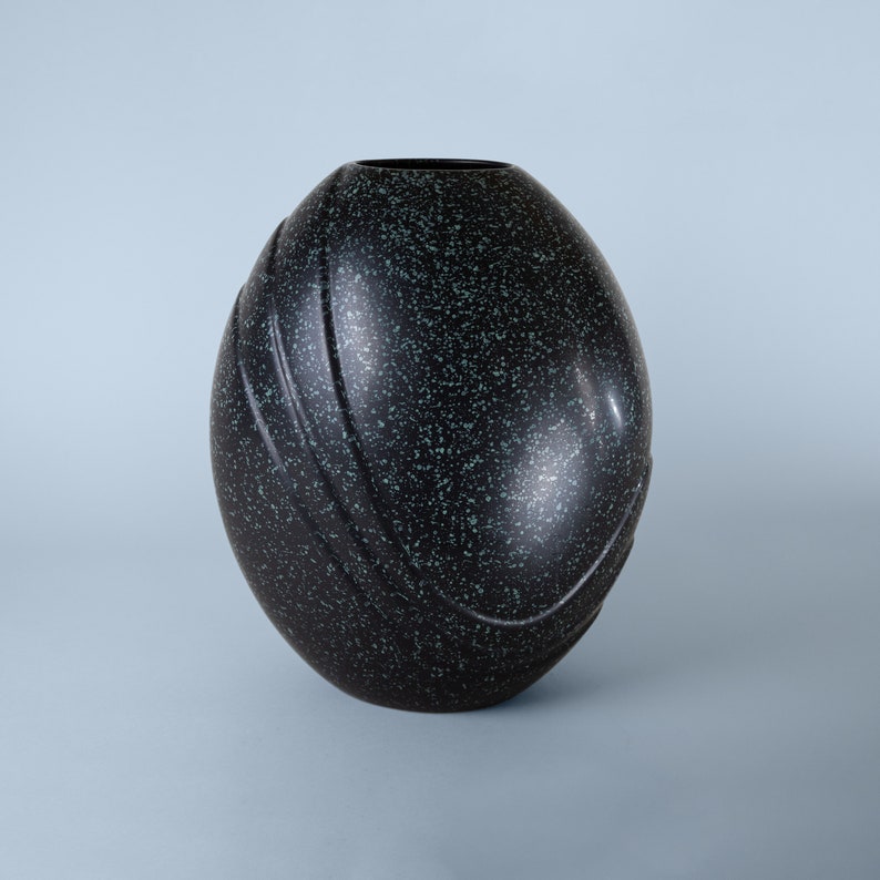 May include: A black and green speckled ceramic vase with a rounded, egg-shaped design.