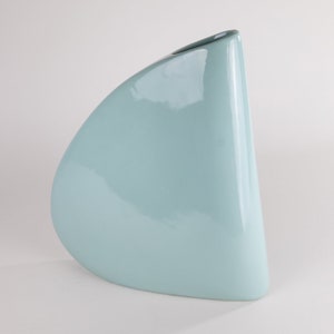 May include: A light blue ceramic vase with a unique, asymmetrical shape. The vase has a smooth, glossy finish.