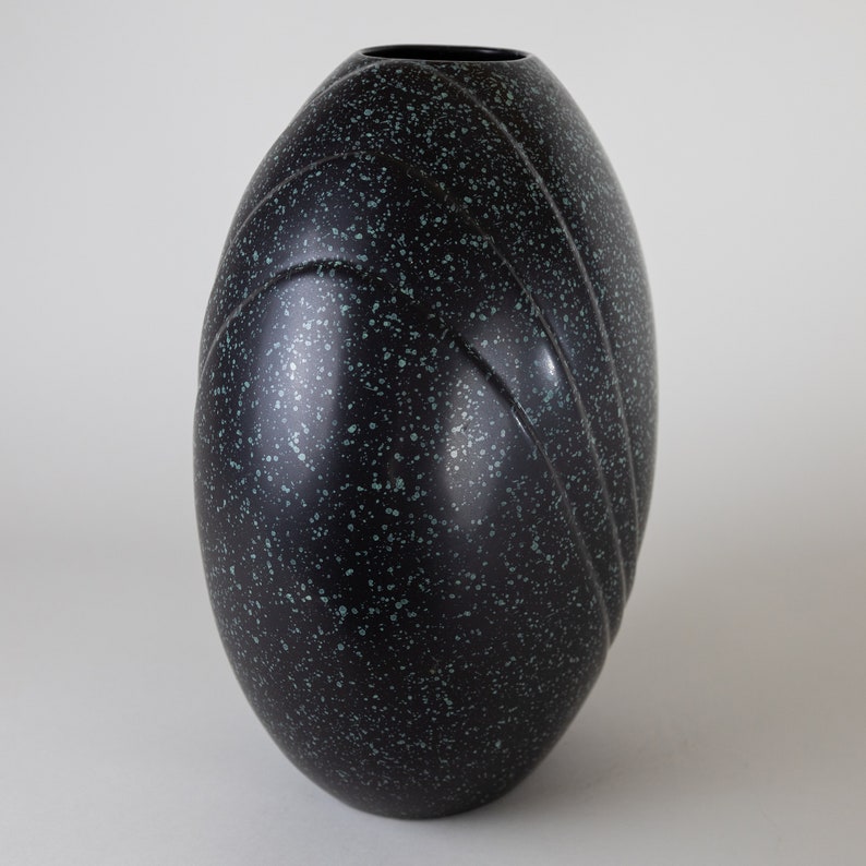 May include: A black and green speckled ceramic vase with a rounded, egg-shaped design. The vase has a smooth, glossy finish and features subtle, raised lines.