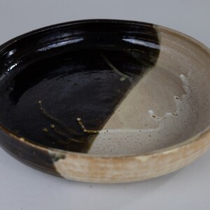 May include: A ceramic bowl with a black and white glaze. The bowl is round and has a slightly raised rim.