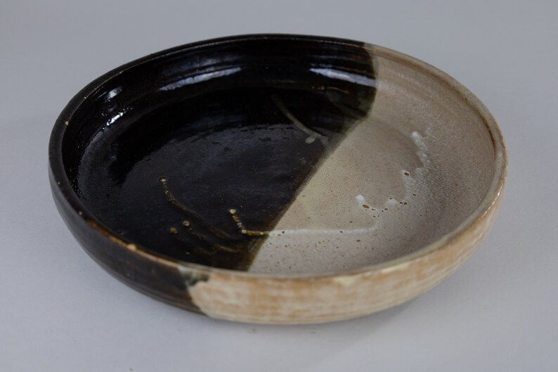 May include: A ceramic bowl with a black and white glaze. The bowl is round and has a slightly raised rim.