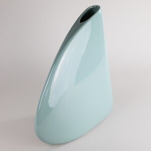 May include: A light blue ceramic vase with a unique, triangular shape and a smooth, glossy finish.