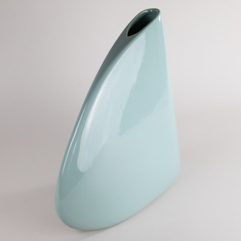 May include: A light blue ceramic vase with a unique, triangular shape and a smooth, glossy finish.