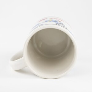 May include: White ceramic mug with a blue and red design. The mug has a handle and is empty.